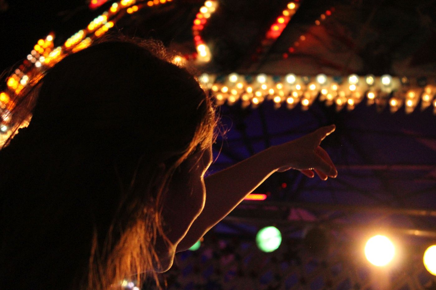 Eine Person auf einem Jahrmarkt, sie zeigt von der Kamera weggedreht auf ein Licht